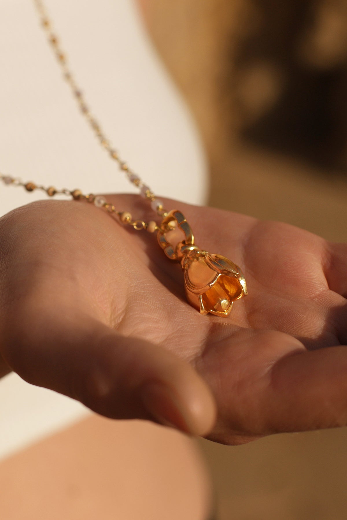 Spiritual jewelry collection: Gloria from Berlin wears a golden lotus bell pendant, a symbol of security, on a gemstone necklace.
